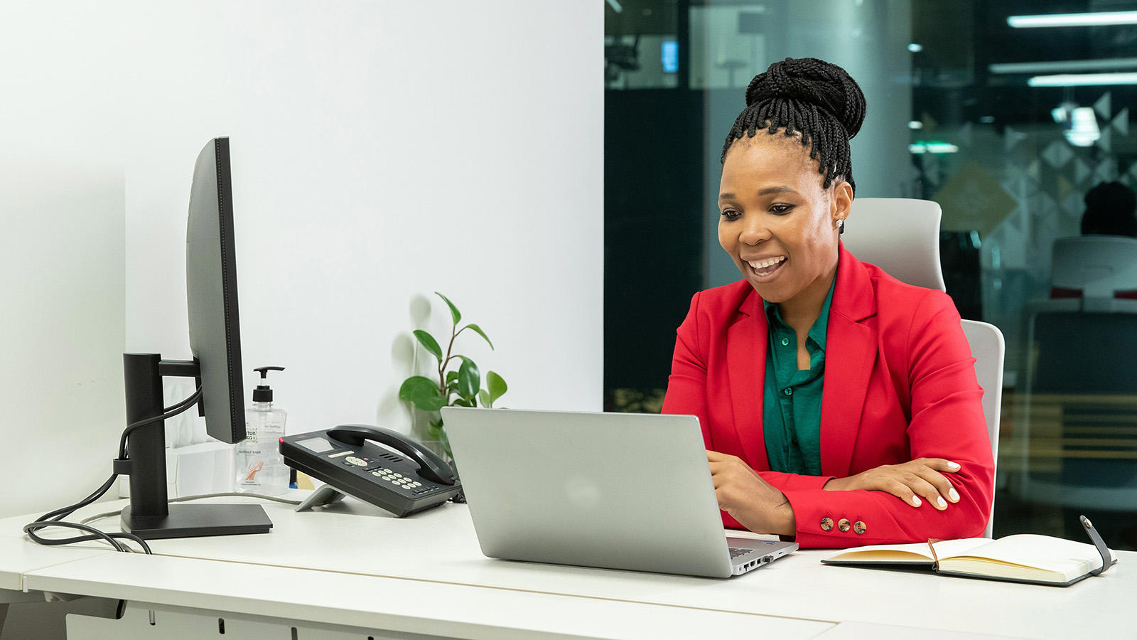 a woman in red jacket sitting at a desk with a laptop
