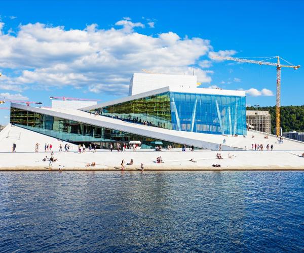 a building with a glass wall and a large building with a crane and a blue sky with clouds