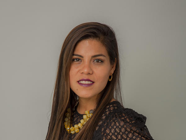 una persona con cabello largo y castaño que lleva una blusa de encaje negro y un collar amarillo