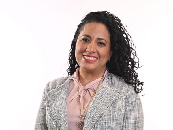 a person with long curly hair wearing a gray jacket and pink shirt